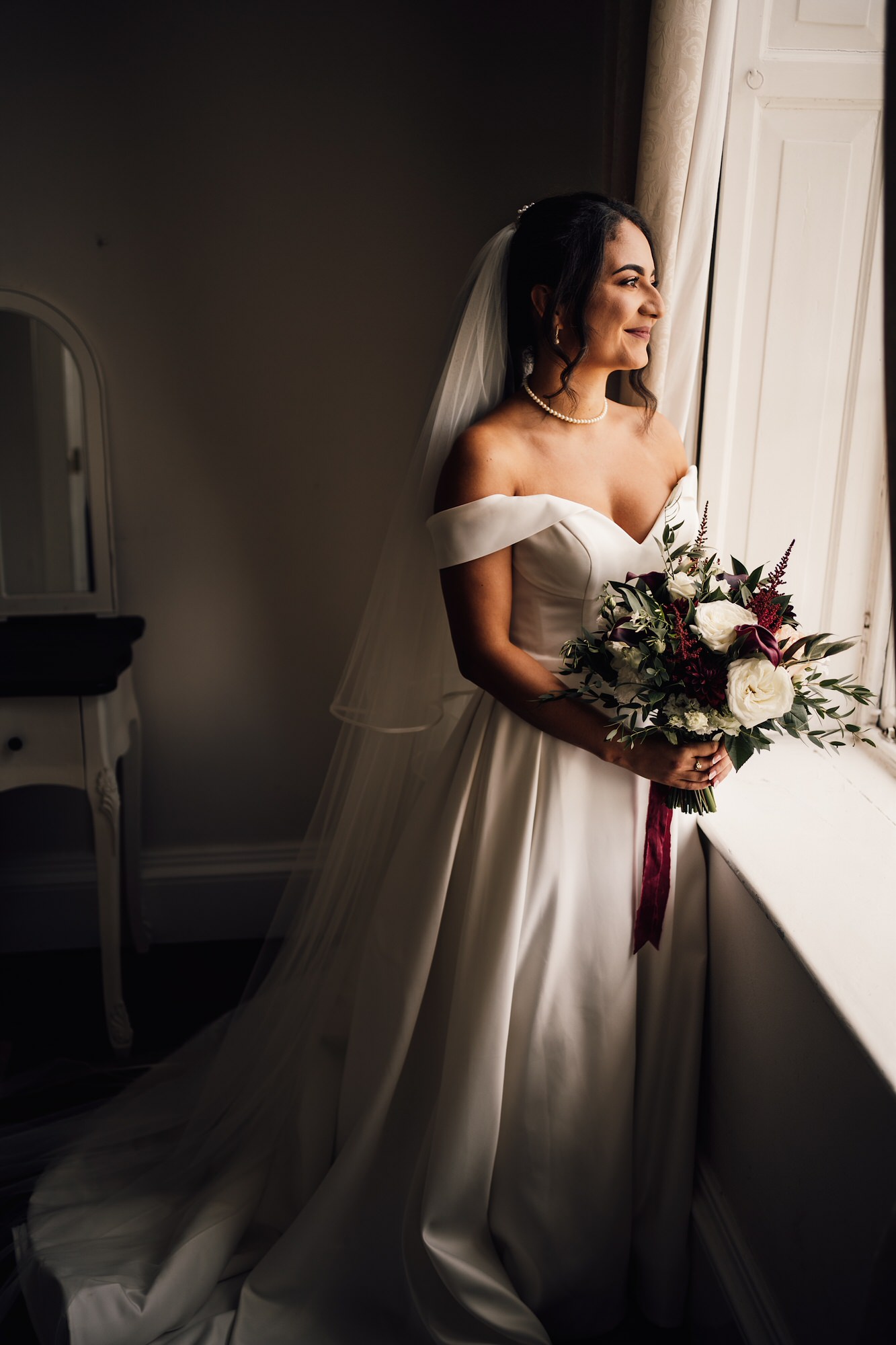 Photo of bride holding bouquet of flowers and looking out of the window