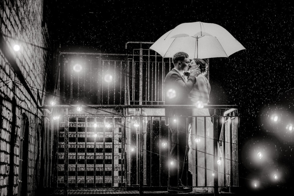 winter wedding portrait of bride and groom standing underneath an umbrella in the rain 