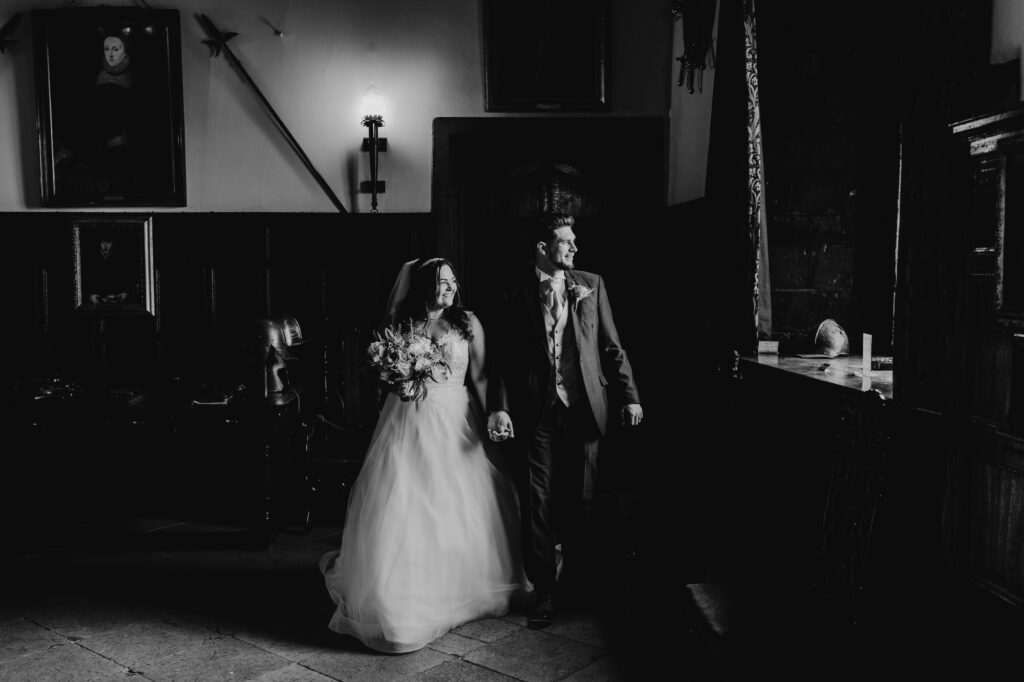 moody black and white portrait of bride and groom standing next to a window with natural light