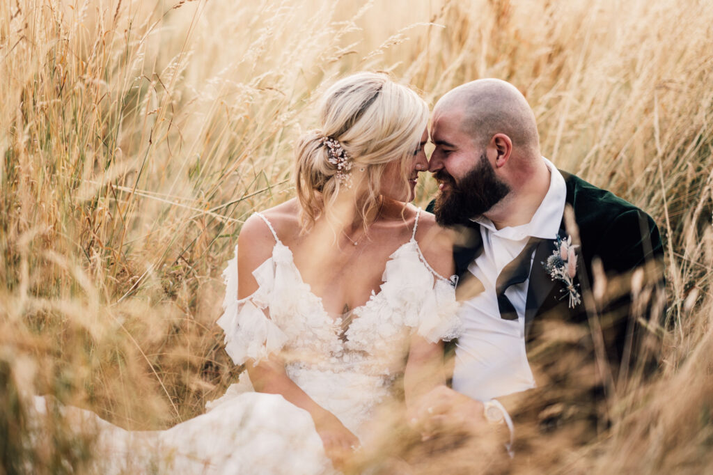 portrait of bride and groom at sunset, sat in a golden wheat field with natural light